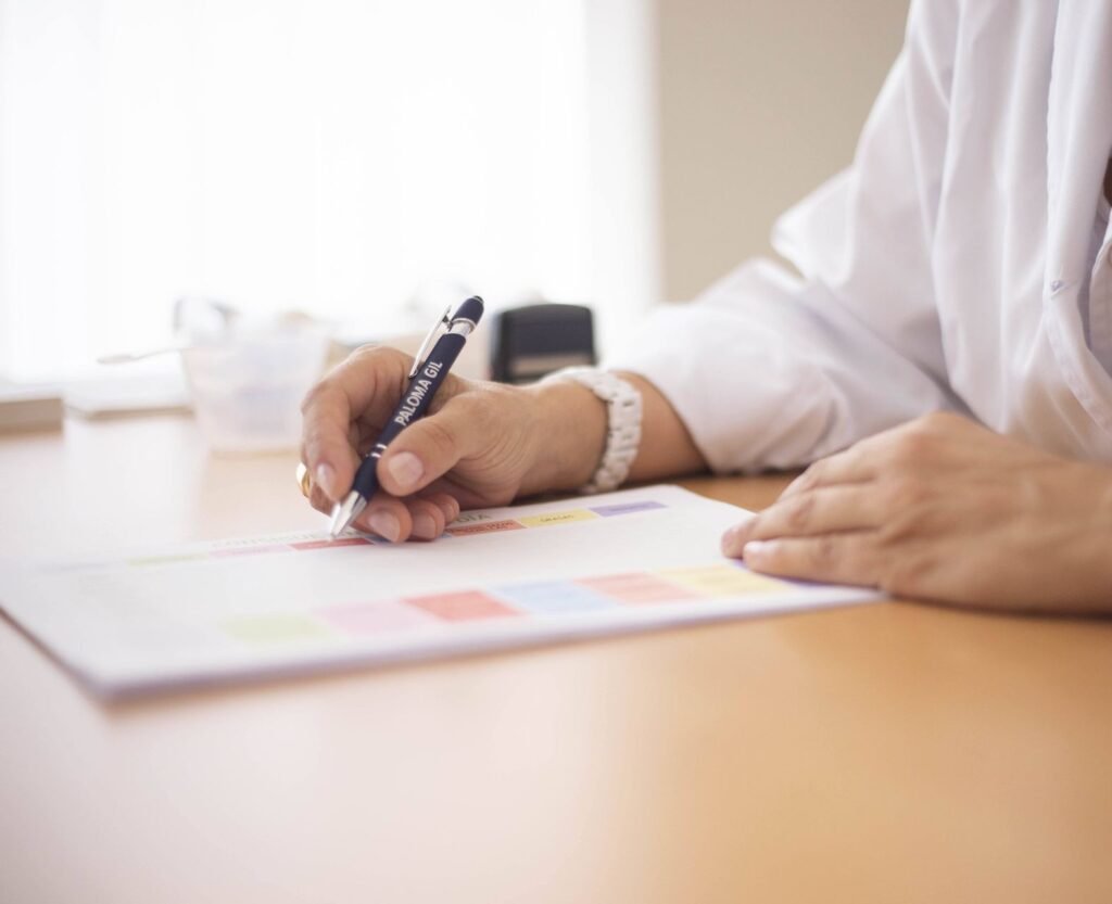 Main d'un médecin en blouse blanche qui écrit à son bureau, lumière naturelle
