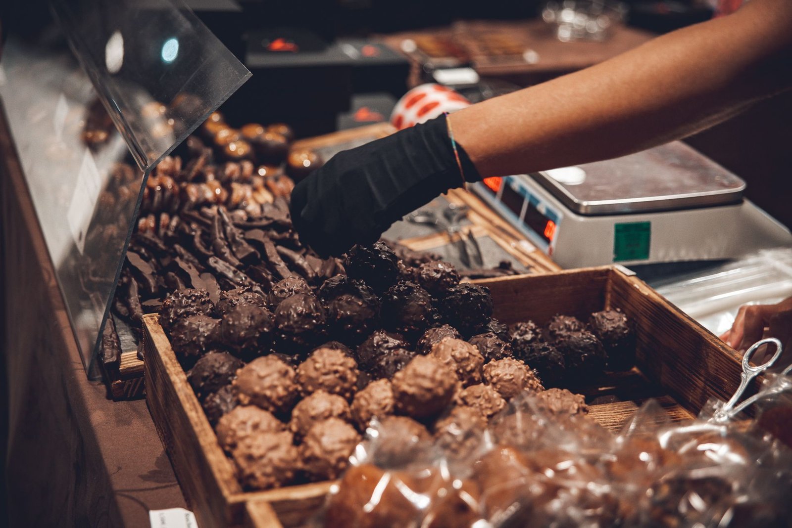 Main gantée qui choisit des truffes au chocolat dans une vitrine de chocolatier